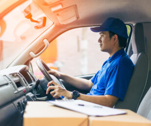 Young handsome delivery man driving his van with packages on the front seat